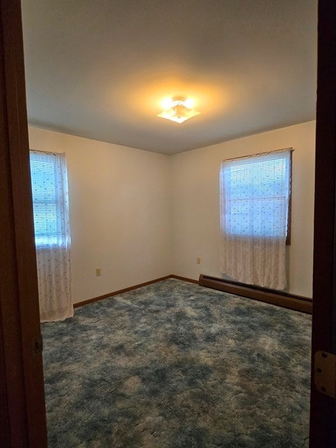 carpeted spare room featuring a baseboard heating unit