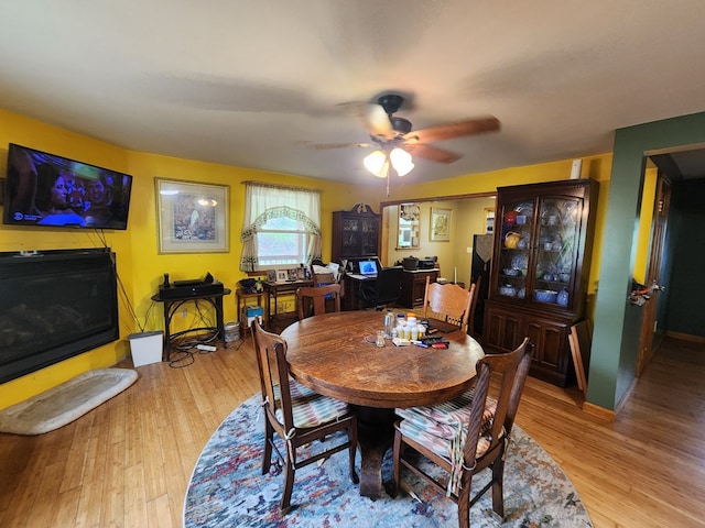 dining space with a fireplace, ceiling fan, and light hardwood / wood-style flooring