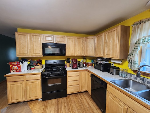 kitchen with light brown cabinetry, sink, black appliances, tile countertops, and light hardwood / wood-style floors