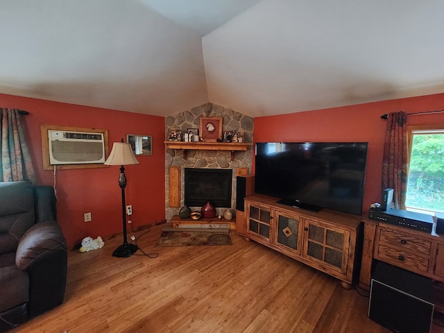 living room with hardwood / wood-style flooring, vaulted ceiling, a wall mounted AC, and a stone fireplace