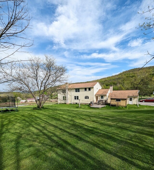 back of house with a lawn, a deck, and a trampoline