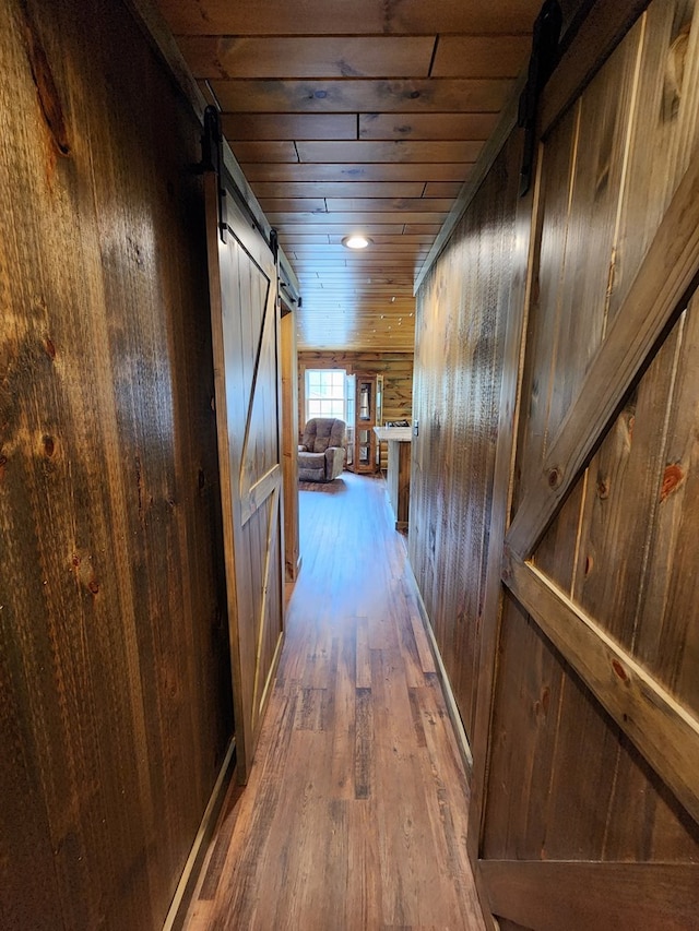 corridor with a barn door, wooden walls, dark wood-type flooring, and wood ceiling