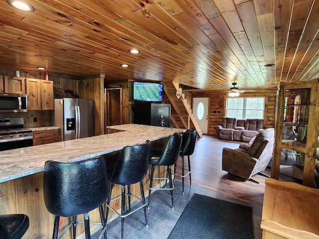 kitchen with appliances with stainless steel finishes, light stone counters, rustic walls, wood ceiling, and wood walls