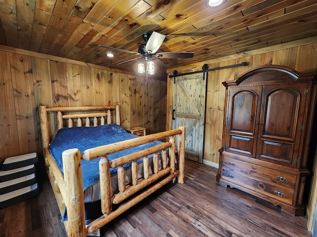 bedroom with wood walls, wooden ceiling, ceiling fan, a barn door, and dark hardwood / wood-style flooring