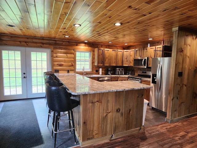 kitchen with light stone countertops, appliances with stainless steel finishes, french doors, rustic walls, and wood ceiling