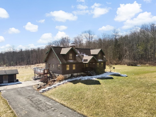 log home featuring a forest view, log exterior, a front yard, a chimney, and driveway