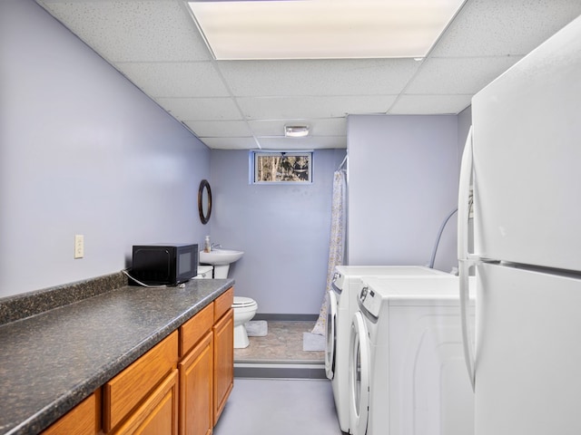 interior space featuring a shower with curtain, baseboards, a drop ceiling, toilet, and independent washer and dryer