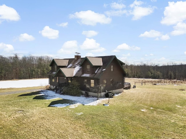 view of home's exterior with log siding, a lawn, a wooded view, and a chimney