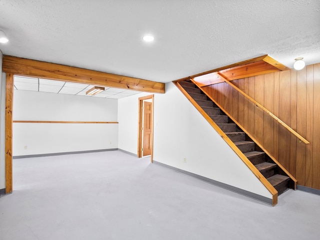 finished basement with stairway, baseboards, a textured ceiling, and wooden walls