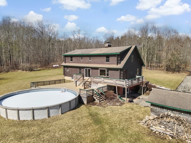 back of house featuring a wooded view, log siding, a yard, a deck, and an empty pool