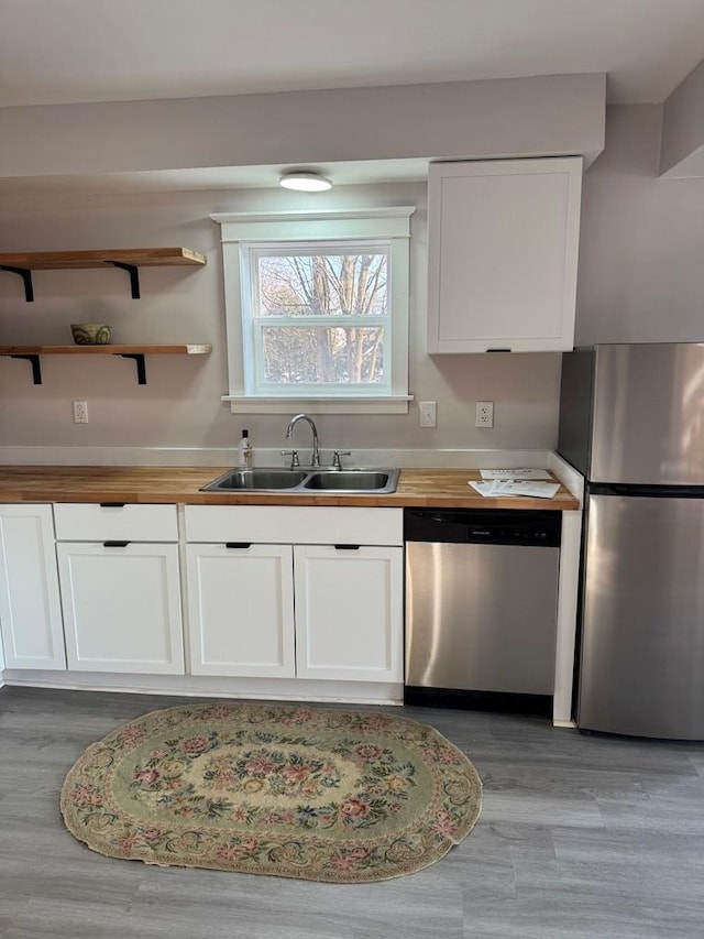 kitchen with a sink, stainless steel appliances, butcher block countertops, and white cabinetry