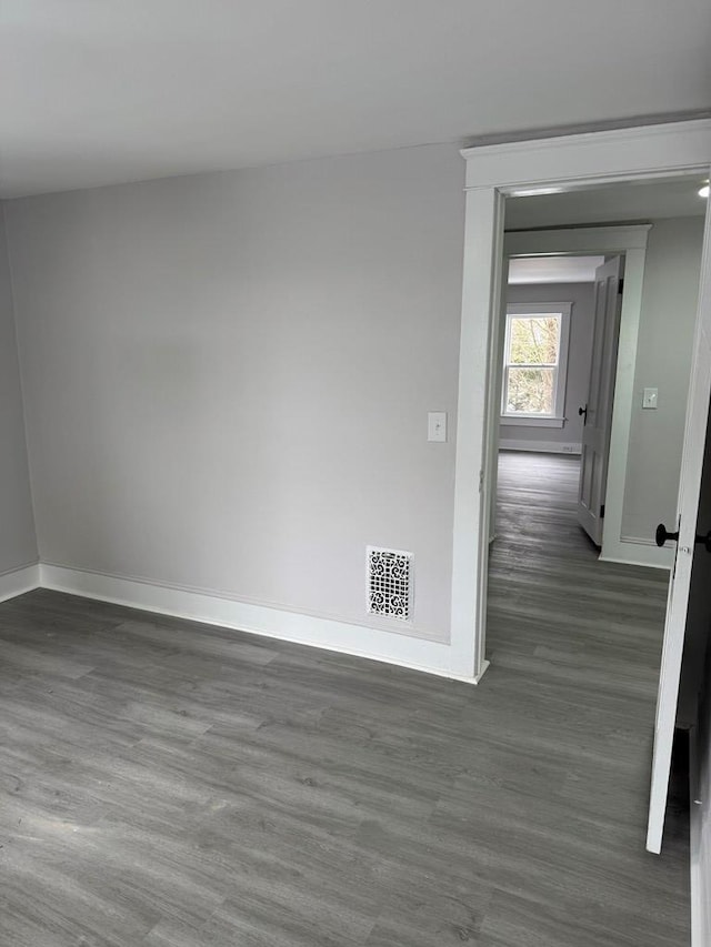 empty room featuring dark wood-type flooring, baseboards, and visible vents