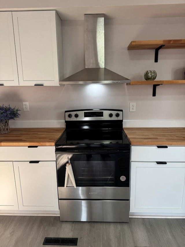 kitchen with wood finished floors, electric stove, wood counters, white cabinetry, and wall chimney range hood