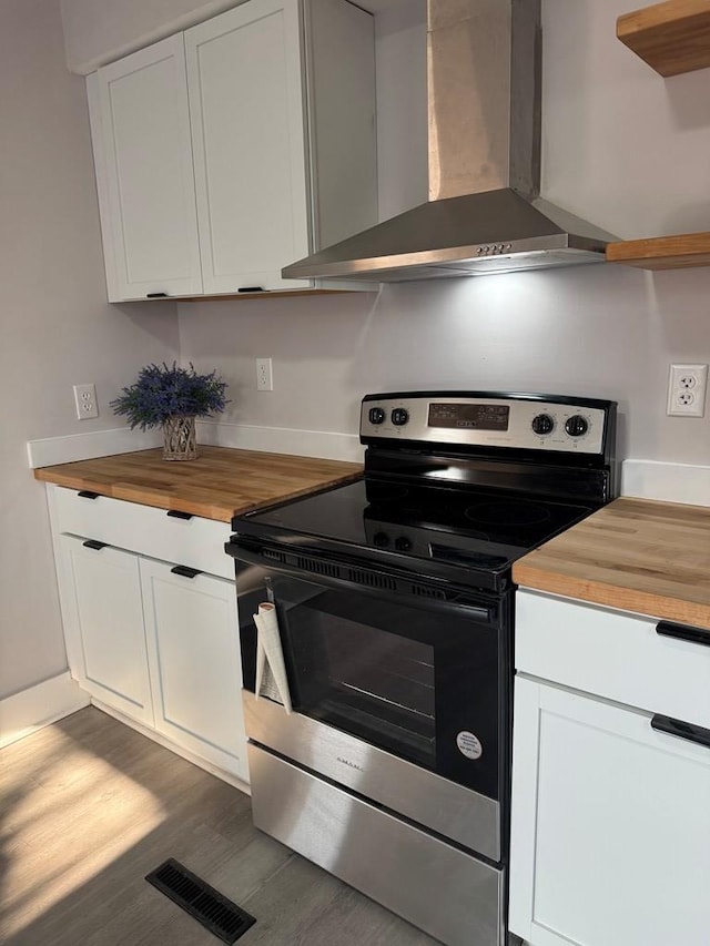 kitchen featuring visible vents, butcher block countertops, stainless steel range with electric stovetop, white cabinetry, and wall chimney range hood