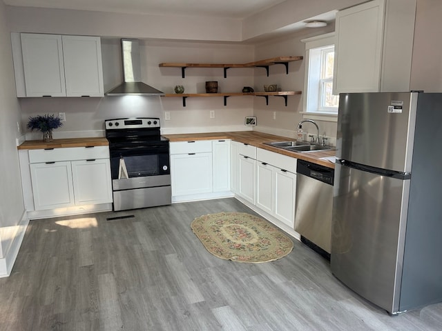 kitchen with a sink, appliances with stainless steel finishes, wall chimney exhaust hood, and butcher block counters