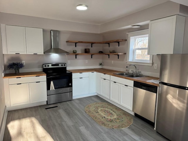 kitchen featuring a sink, white cabinetry, appliances with stainless steel finishes, wall chimney exhaust hood, and wooden counters