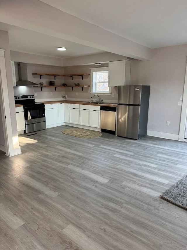 kitchen with light wood finished floors, wall chimney range hood, appliances with stainless steel finishes, white cabinets, and open shelves