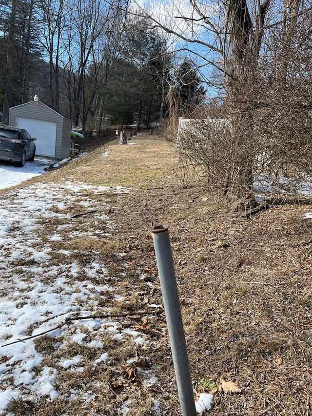 snowy yard featuring driveway, an outdoor structure, and a garage