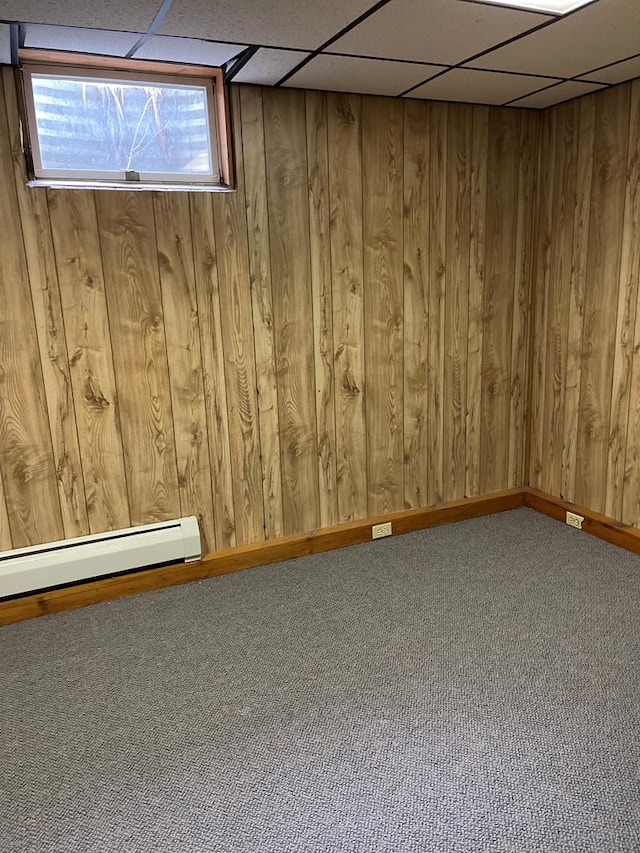 basement featuring wooden walls, a drop ceiling, and carpet floors