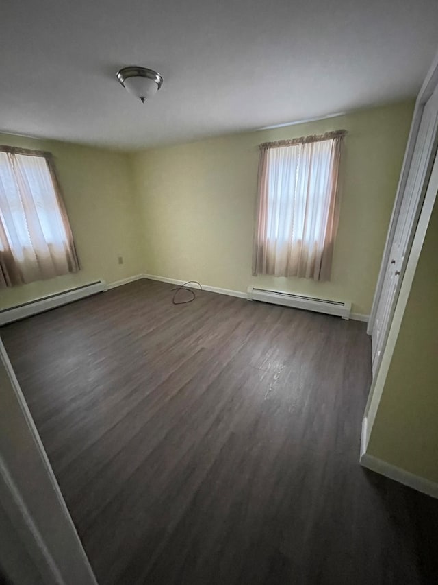 empty room featuring baseboard heating and dark hardwood / wood-style floors