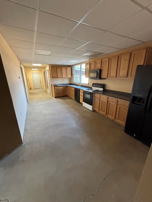 kitchen with brown cabinets, black appliances, a drop ceiling, dark countertops, and concrete floors