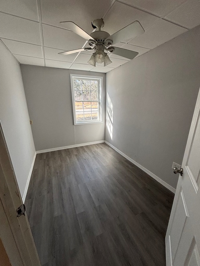 unfurnished bedroom featuring a drop ceiling, baseboards, dark wood-type flooring, and ceiling fan