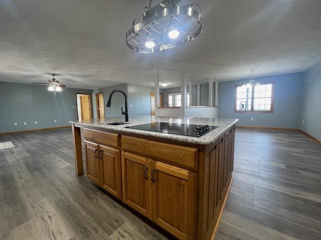 kitchen featuring black electric stovetop, ceiling fan with notable chandelier, sink, dark hardwood / wood-style floors, and an island with sink