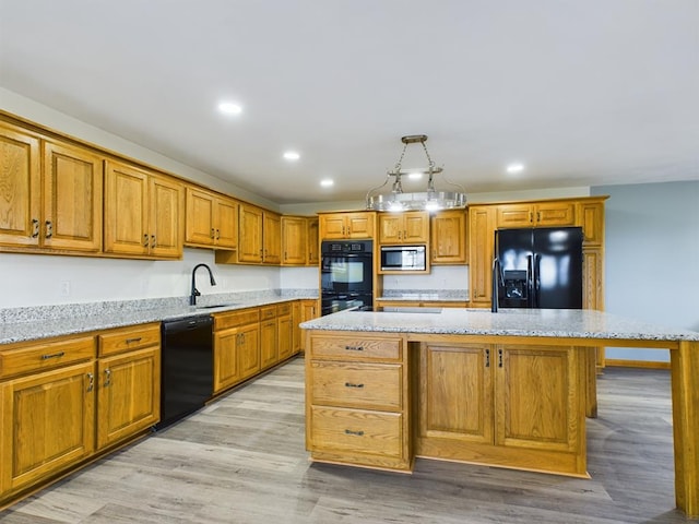 kitchen featuring a center island, sink, decorative light fixtures, black appliances, and light wood-type flooring