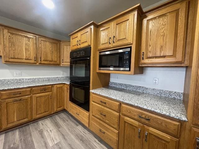 kitchen featuring light stone countertops, stainless steel microwave, light hardwood / wood-style floors, and black double oven