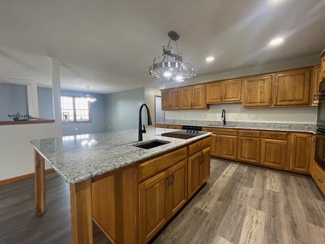 kitchen with hanging light fixtures, hardwood / wood-style floors, a kitchen island with sink, and sink