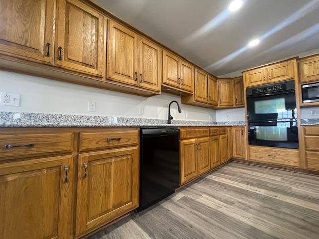 kitchen with black appliances, light stone countertops, light wood-type flooring, and sink