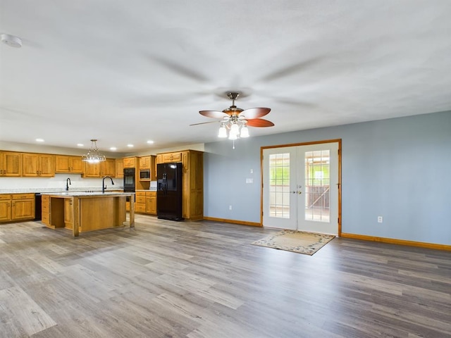 kitchen with french doors, hanging light fixtures, an island with sink, light hardwood / wood-style floors, and black fridge with ice dispenser