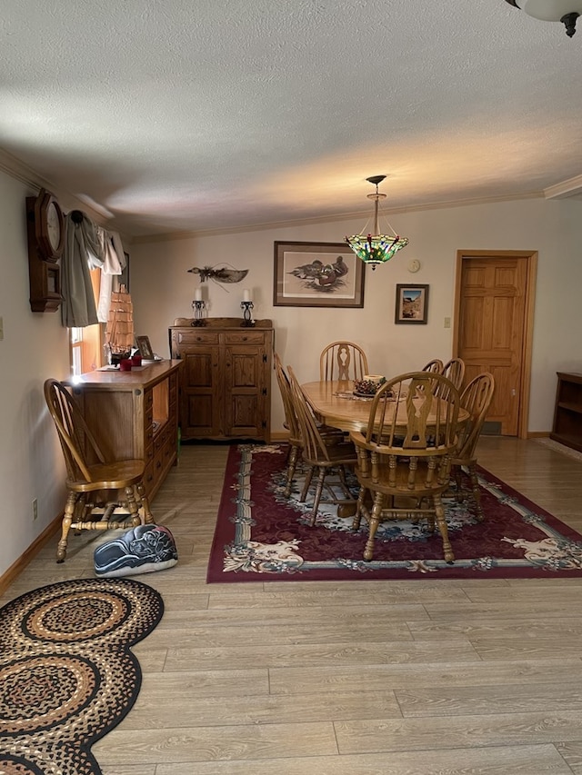 dining area with a textured ceiling, light wood-type flooring, and crown molding