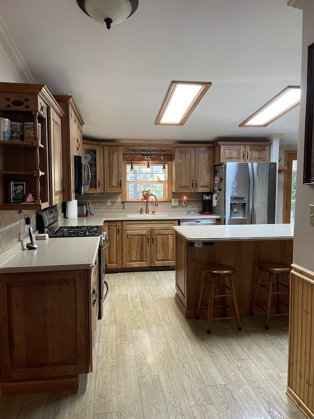 kitchen featuring sink, stainless steel appliances, crown molding, light hardwood / wood-style floors, and a breakfast bar