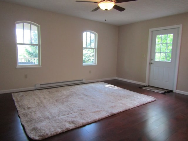 empty room featuring ceiling fan, dark wood-type flooring, and a baseboard heating unit