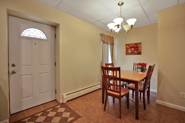 tiled dining space with a drop ceiling, a baseboard heating unit, and a notable chandelier