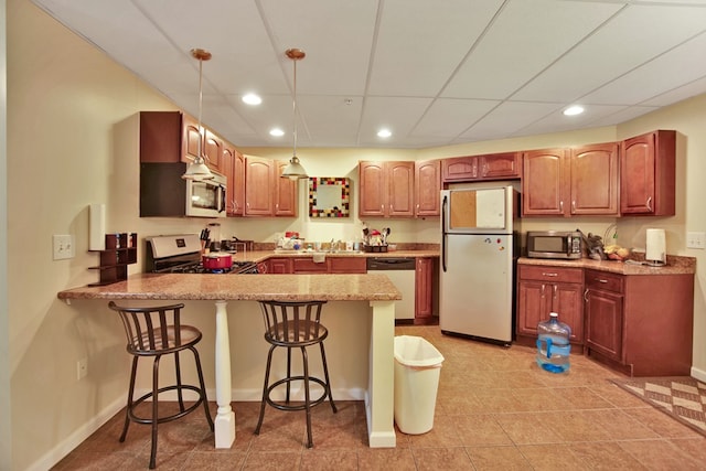 kitchen with kitchen peninsula, hanging light fixtures, light stone counters, appliances with stainless steel finishes, and a kitchen bar