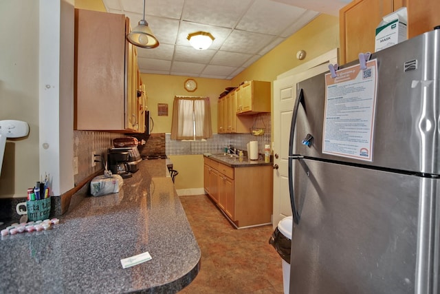 kitchen with tasteful backsplash, hanging light fixtures, a drop ceiling, stainless steel refrigerator, and sink