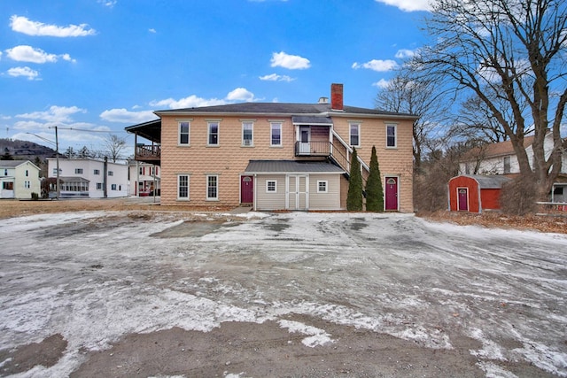 snow covered back of property featuring a balcony and a storage shed