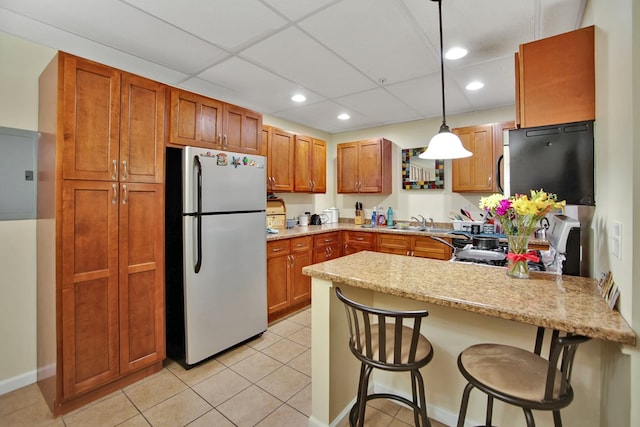 kitchen featuring a kitchen bar, light tile patterned floors, decorative light fixtures, stainless steel fridge, and kitchen peninsula