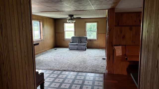 sitting room featuring carpet floors, wooden walls, ceiling fan, and a healthy amount of sunlight