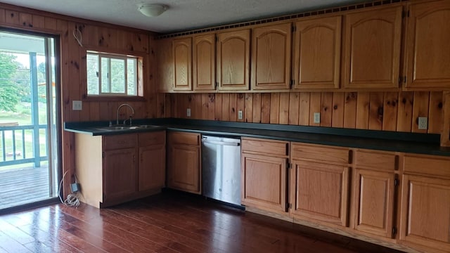 kitchen with wood walls, dark wood-type flooring, sink, stainless steel dishwasher, and a textured ceiling