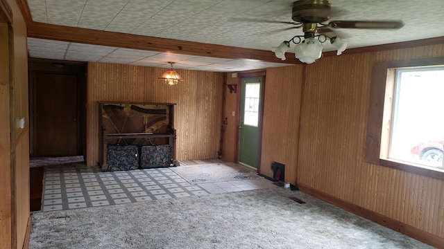 unfurnished living room featuring light colored carpet, plenty of natural light, wooden walls, and ceiling fan