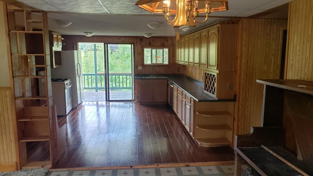 kitchen with an inviting chandelier, sink, wooden walls, dark hardwood / wood-style flooring, and white range with gas stovetop