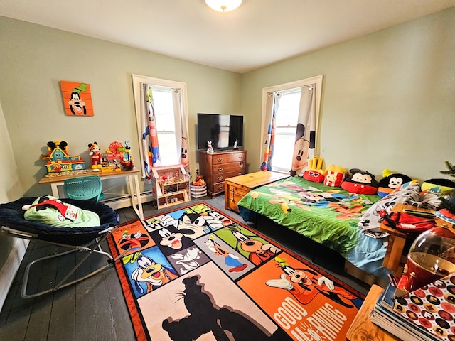 bedroom with multiple windows, a baseboard heating unit, and hardwood / wood-style flooring