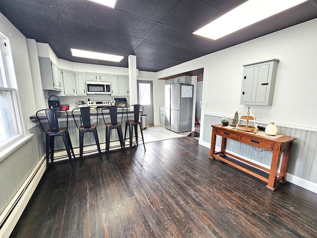 kitchen with kitchen peninsula, stainless steel appliances, baseboard heating, dark wood-type flooring, and a breakfast bar area