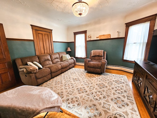 living room with a chandelier, light wood-type flooring, a baseboard radiator, and a healthy amount of sunlight