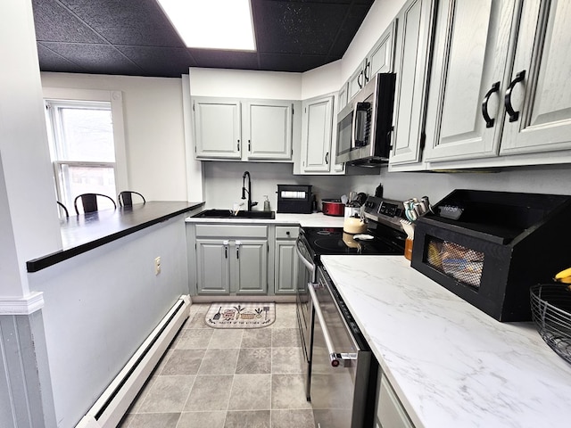 kitchen with gray cabinetry, a baseboard heating unit, sink, light stone countertops, and stainless steel appliances