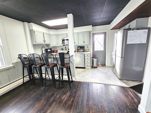 kitchen featuring stainless steel appliances, light hardwood / wood-style flooring, a drop ceiling, and a breakfast bar area