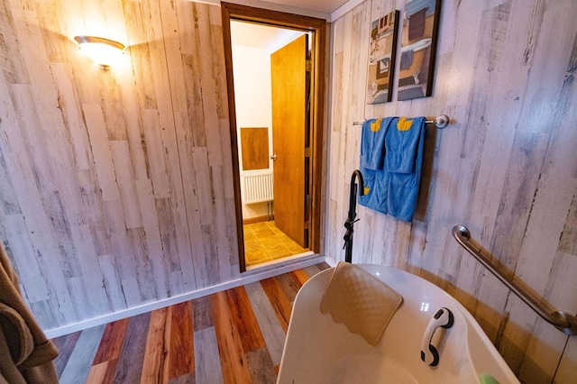 bathroom with a tub to relax in, hardwood / wood-style floors, and wooden walls